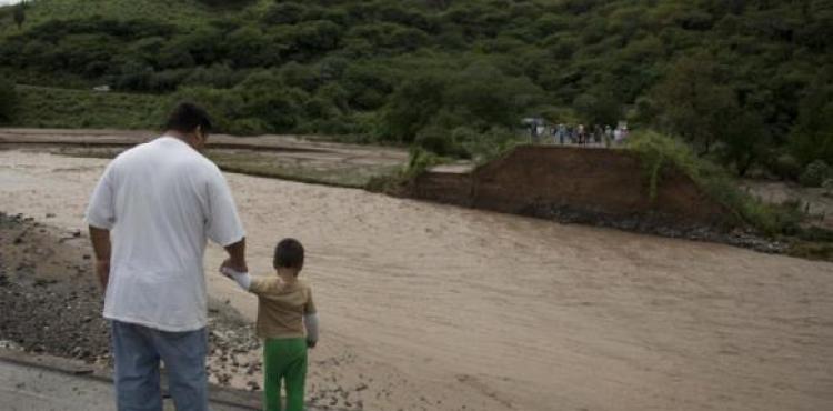  مكسيكيون يقفون أمام جسر مطل على أحد الأنهار سقط إثر إعصار باتريشيا