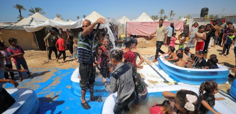 نازحون يحاولون تخفيف موجة الحر عن أطفالهم من خلال مسابح صغيرة أمام الخيام في دير البلح