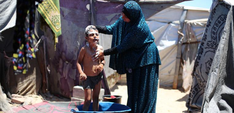 أم فلسطينية تحمم طفلها داخل خيمه نزوح لتخفيف من حرارة الصيف وحرارة الخيام في مخيم البريج
